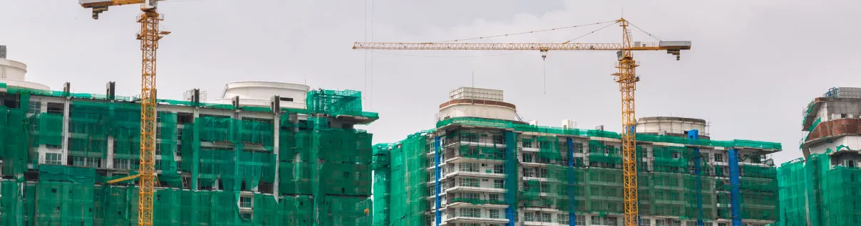 Cranes at a construction site and the buildings in the background are covered with debris netting.