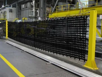 Large industrial netting with black mesh in a manufacturing facility, propped up by yellow installation poles.