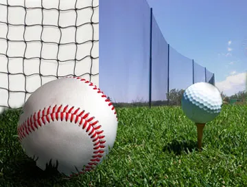 Baseball close-up beside a white net with a golf ball on a tee in the background, set against a green grass field and clear blue sky.