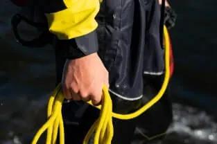 Person in yellow and black holding yellow kevlar rope by the water.