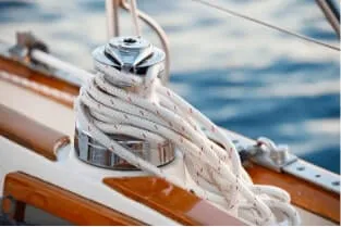 A coiled nylon rope neatly wrapped around a winch on a sailboat, with a view of the boat's deck and the shimmering water in the background.